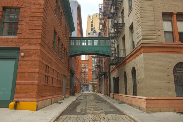 Uma ruela estreita com edifícios de tijolo, uma passarela verde para pedestres e rua de paralelepípedos.