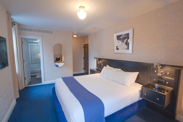 A hotel room with a large bed, a nightstand, a mirror, and a door leading to a bathroom. - The Frederick Hotel Tribeca, a Small Luxury Hotel (New York)
