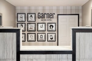 A reception area with a check-in counter, framed artwork on the wall, and a sign reading "Garner AN IHG HOTEL".