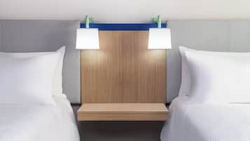 Quarto de hotel com duas camas, cabeceira de madeira e duas luminárias laterais.