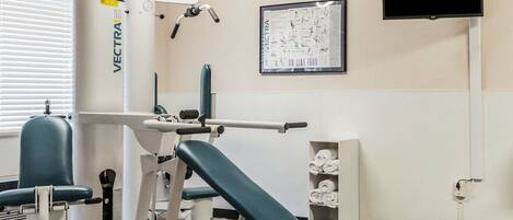 Une salle de sport équipée d’un banc de musculation, d’une machine à développé couché et d’un téléviseur fixé au mur.