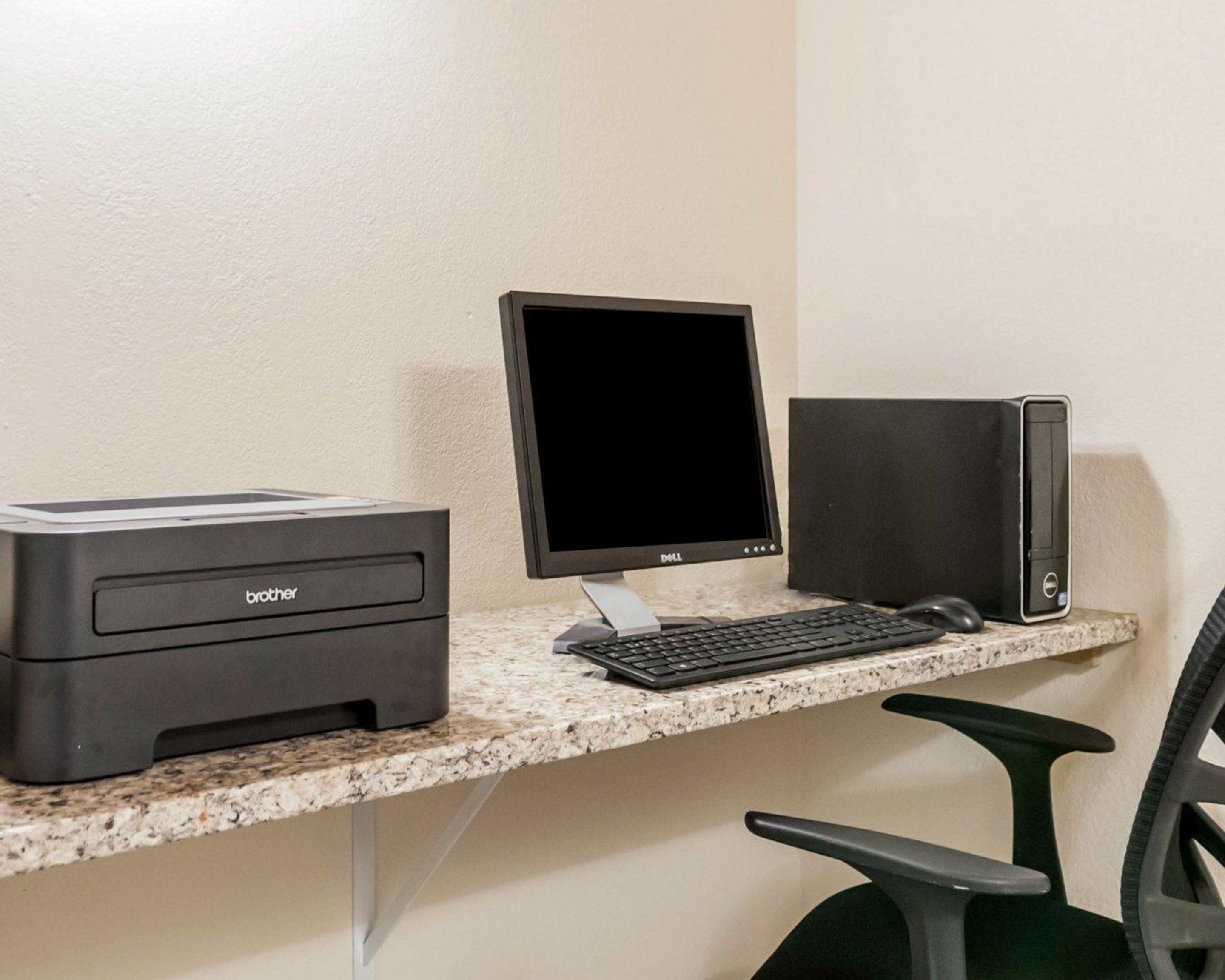 A computer desk with a Brother printer, a Dell monitor, a keyboard, a mouse, and a black desktop computer.