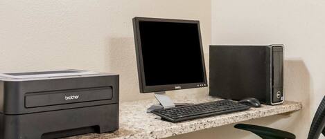 A computer desk with a Brother printer, a Dell monitor, a keyboard, a mouse, and a black desktop computer.
