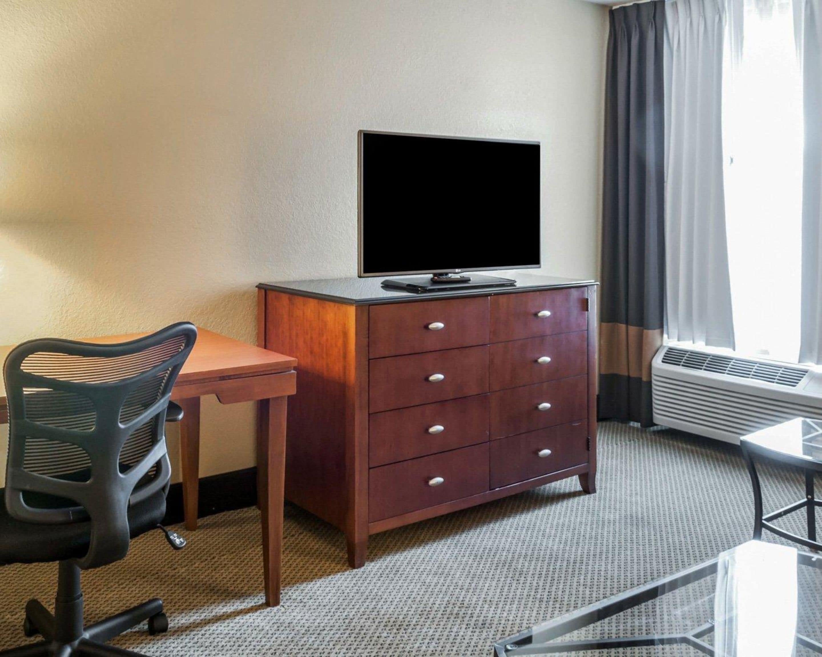 Una habitación de hotel con escritorio, silla, televisor y cómoda.
