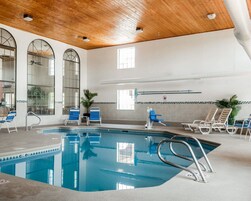 Una piscina interior con agua cristalina, rodeada de sillas de descanso y un techo de madera.