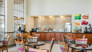 A modern cafe with wooden furniture, a patterned wall, and a counter with various food items. - Quality Inn & Suites Albuquerque West (Albuquerque)