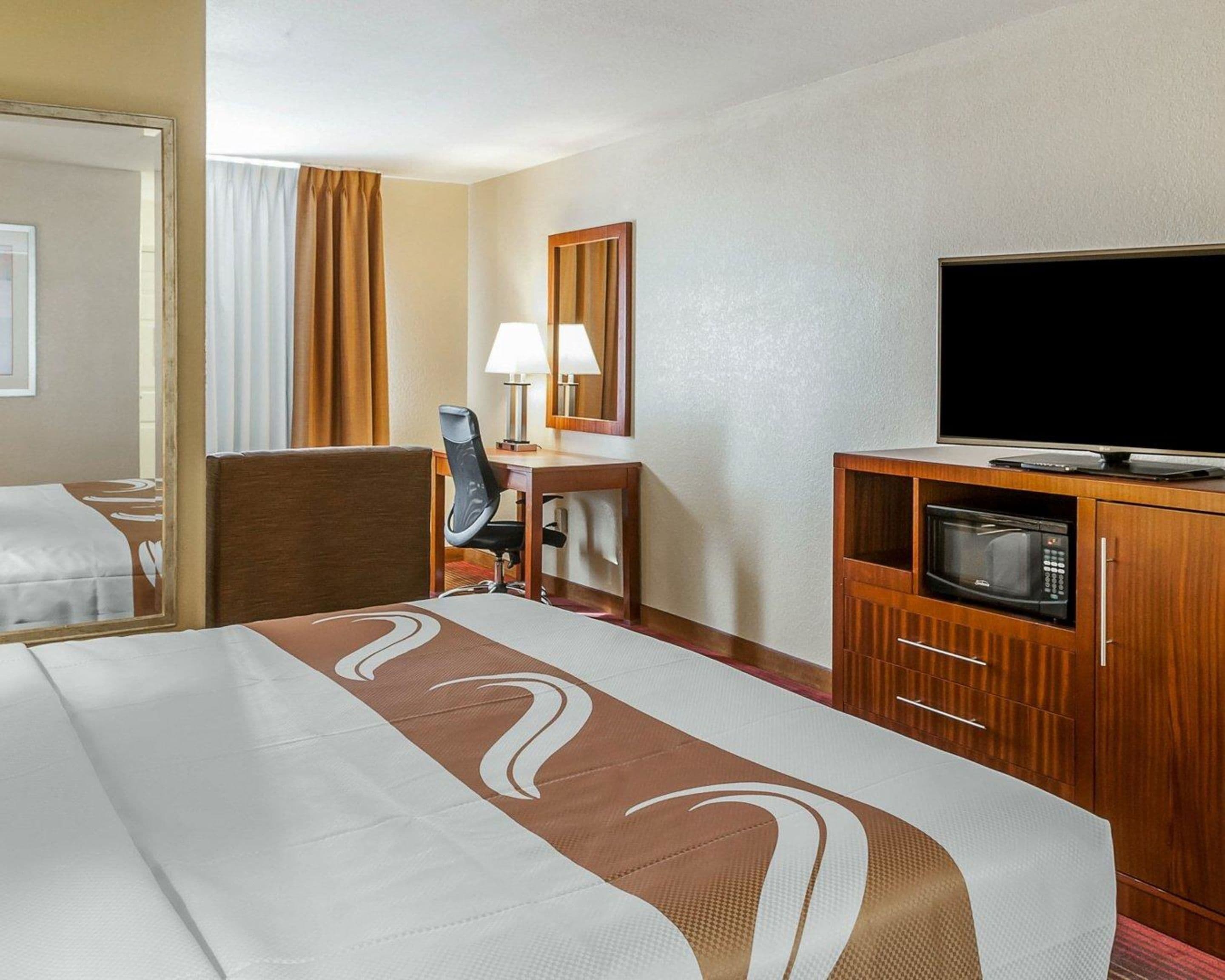 Una habitación de hotel con cama, escritorio, silla, televisor y microondas.