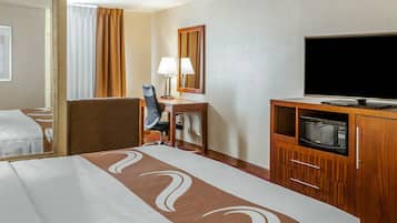 Una habitación de hotel con cama, escritorio, silla, televisor y microondas.