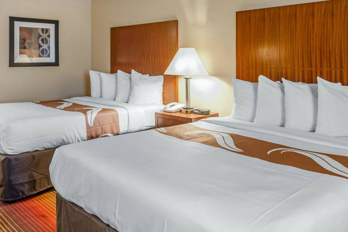 A hotel room with two beds, a nightstand with a lamp, and a framed picture on the wall.