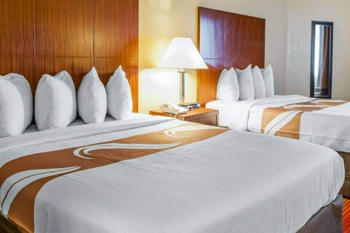A hotel room with two beds, a nightstand with a lamp, and a wooden headboard.