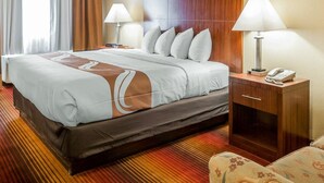A hotel room with a large bed, two bedside lamps, a wooden headboard, a bedside table with a phone, and a patterned armchair. - Quality Inn & Suites Albuquerque West (Albuquerque)