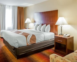 Habitación de hotel con una cama grande, dos lámparas de noche, un cabecero de madera, una mesita de noche con un teléfono y un sillón con estampado.
