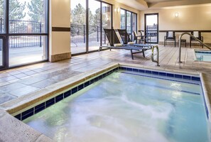 Un espace piscine intérieure chauffée, doté de chaises longues et offrant une vue sur l’extérieur.