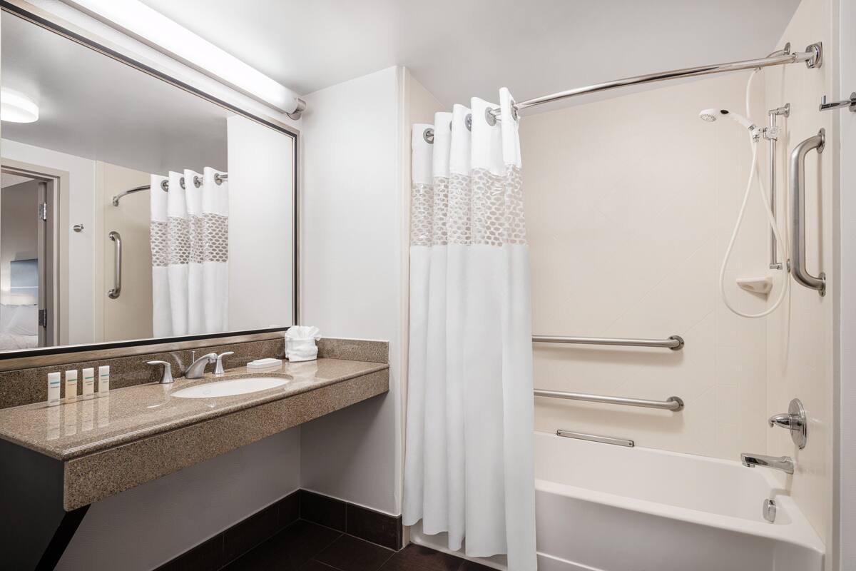 A modern bathroom with a granite countertop, two sinks, a large mirror, a shower with a glass door, and grab bars.