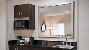 A modern kitchen with dark wooden cabinets, a built-in microwave, a coffee maker, and a sink with a mirror above it. - Hampton Inn Boulder - Louisville (Louisville)