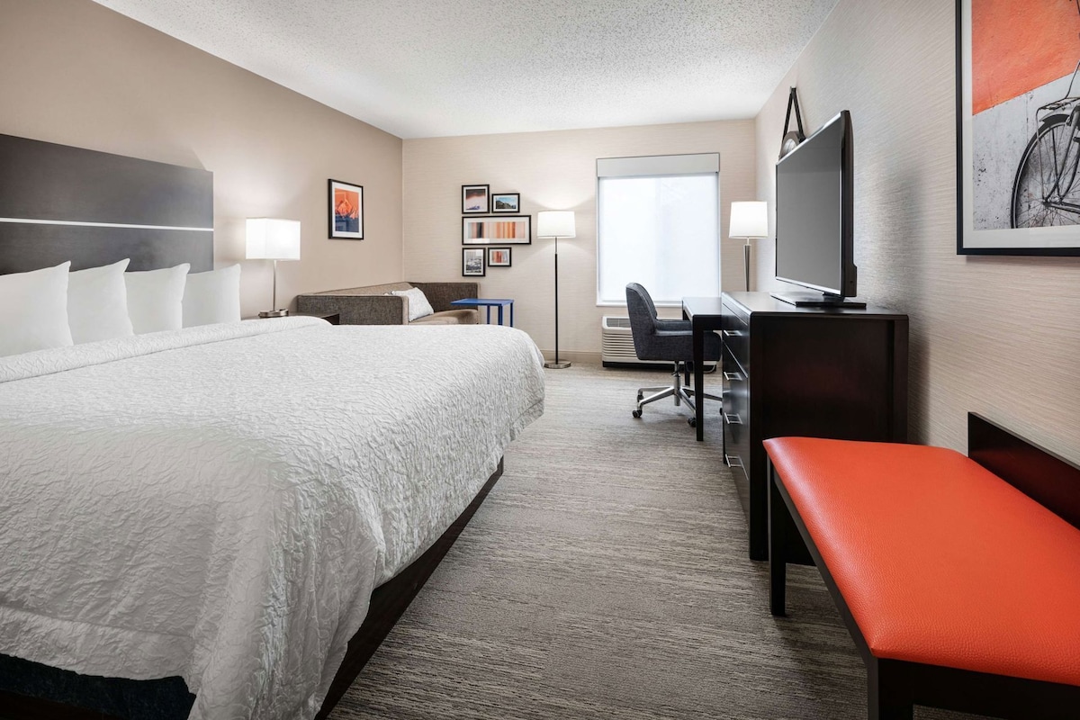A hotel room with a large bed, a desk, a chair, a TV, and a window.
