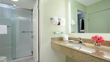 Un baño con cabina de ducha de vidrio, un lavamanos con encimera de mármol y un espejo sobre el lavamanos.