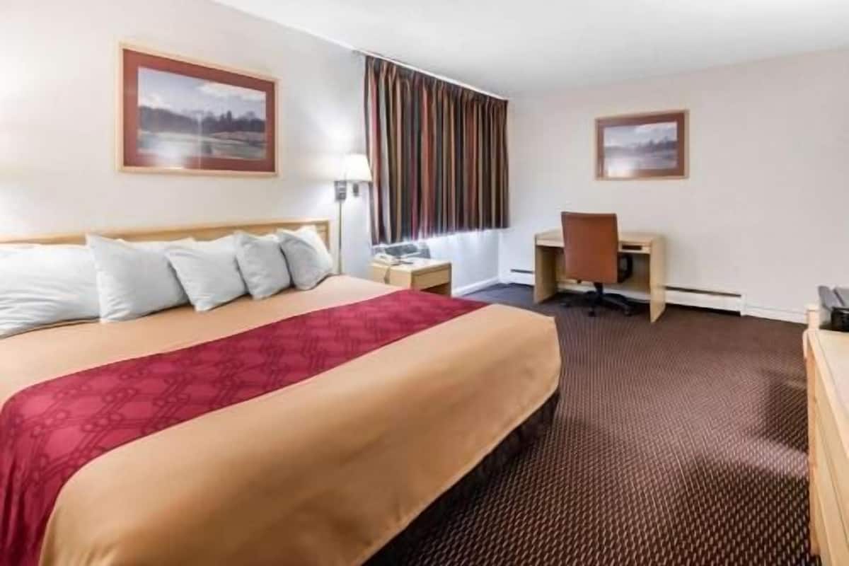 A hotel room with a bed, a desk, a chair, and two framed pictures on the walls.