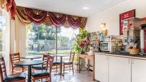 A dining area with wooden chairs and tables, a kitchen with a microwave and coffee maker, and a view of the outdoors. - Econo Lodge Colorado Springs Downtown (Colorado Springs)
