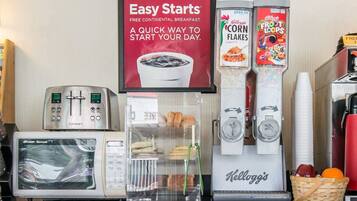 Una barra de desayuno con un tostador Cuisinart, un microondas, un refrigerador con pastelería y dos dispensadores de bebidas Kellogg's.