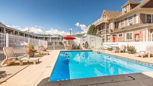 A swimming pool with lounge chairs and a red umbrella, surrounded by a fence and buildings. - Econo Lodge Colorado Springs Downtown (Colorado Springs)