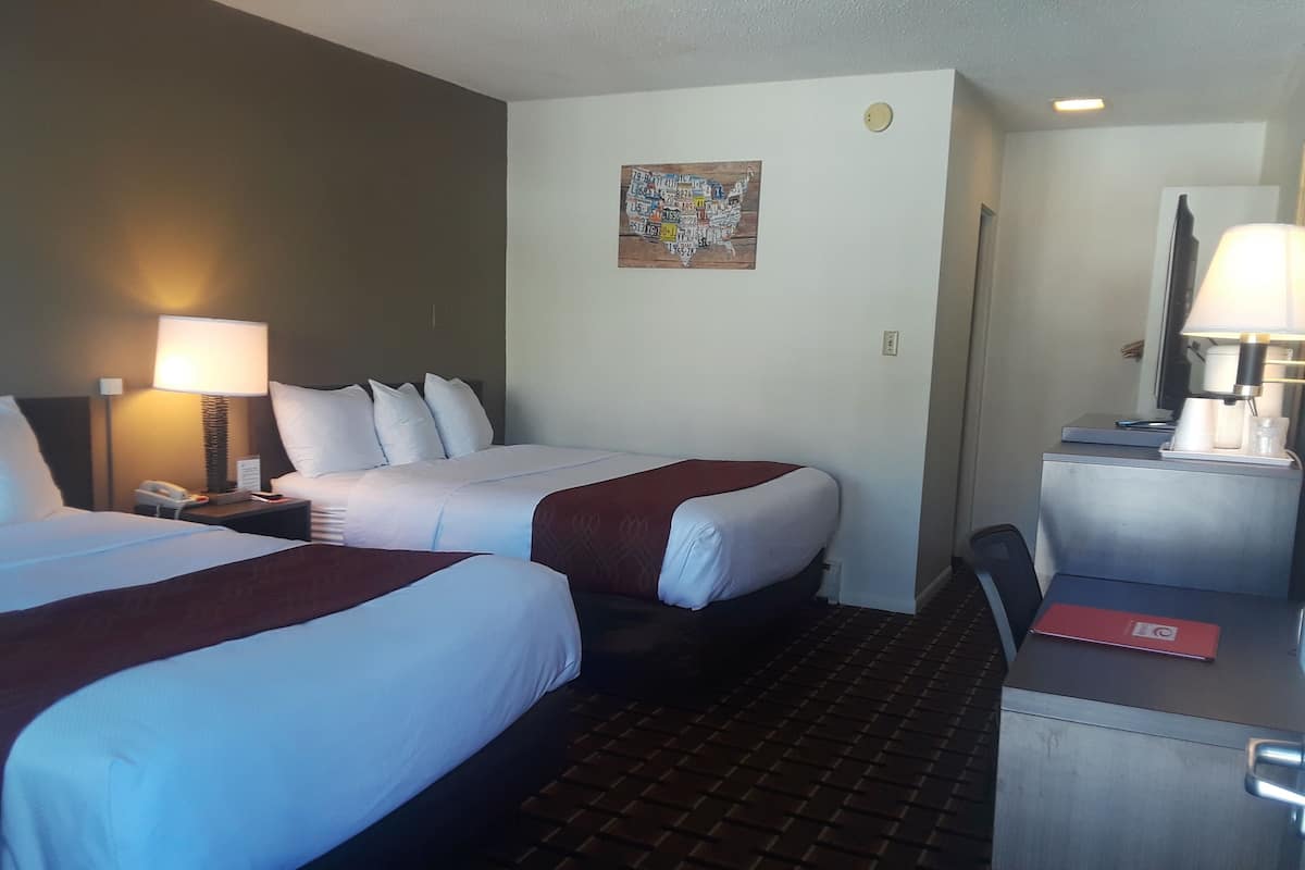 A hotel room with two beds, a desk, a chair, a lamp, a phone, and a wall decoration.