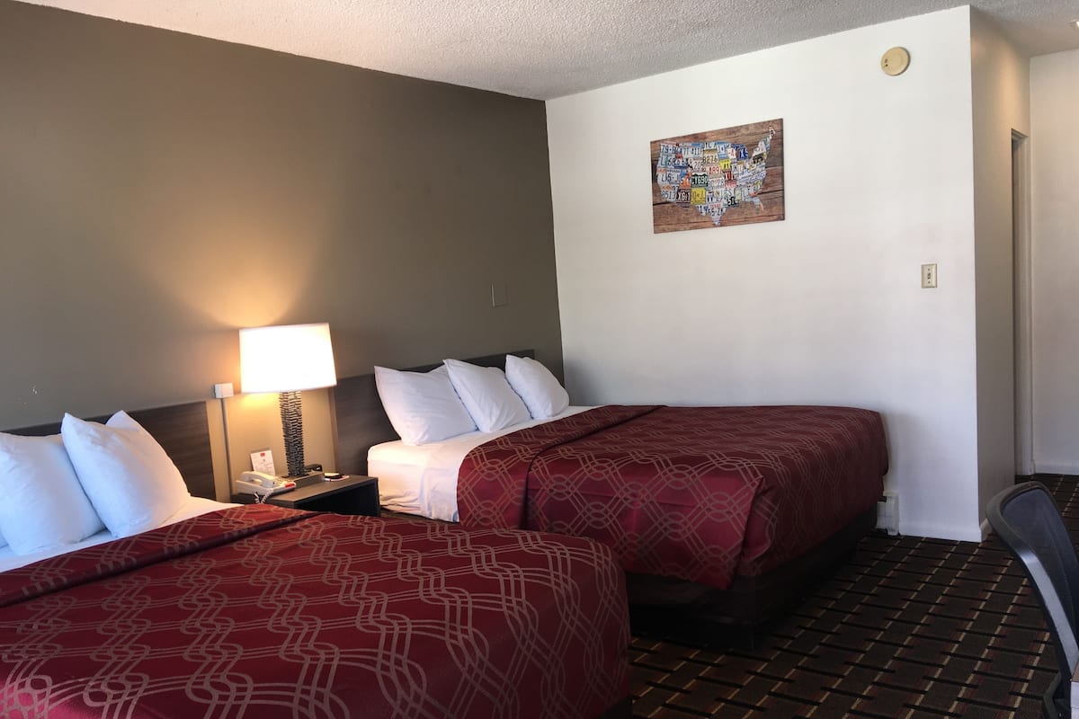 A hotel room with two beds, a nightstand with a lamp, a wall clock, and a map on the wall.
