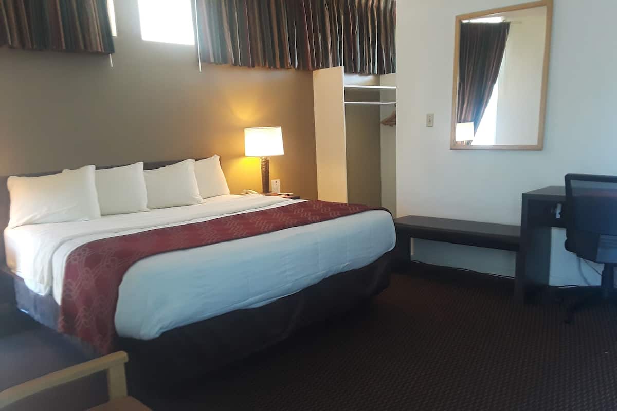 A hotel room with a bed, a desk, a chair, a lamp, and a mirror.