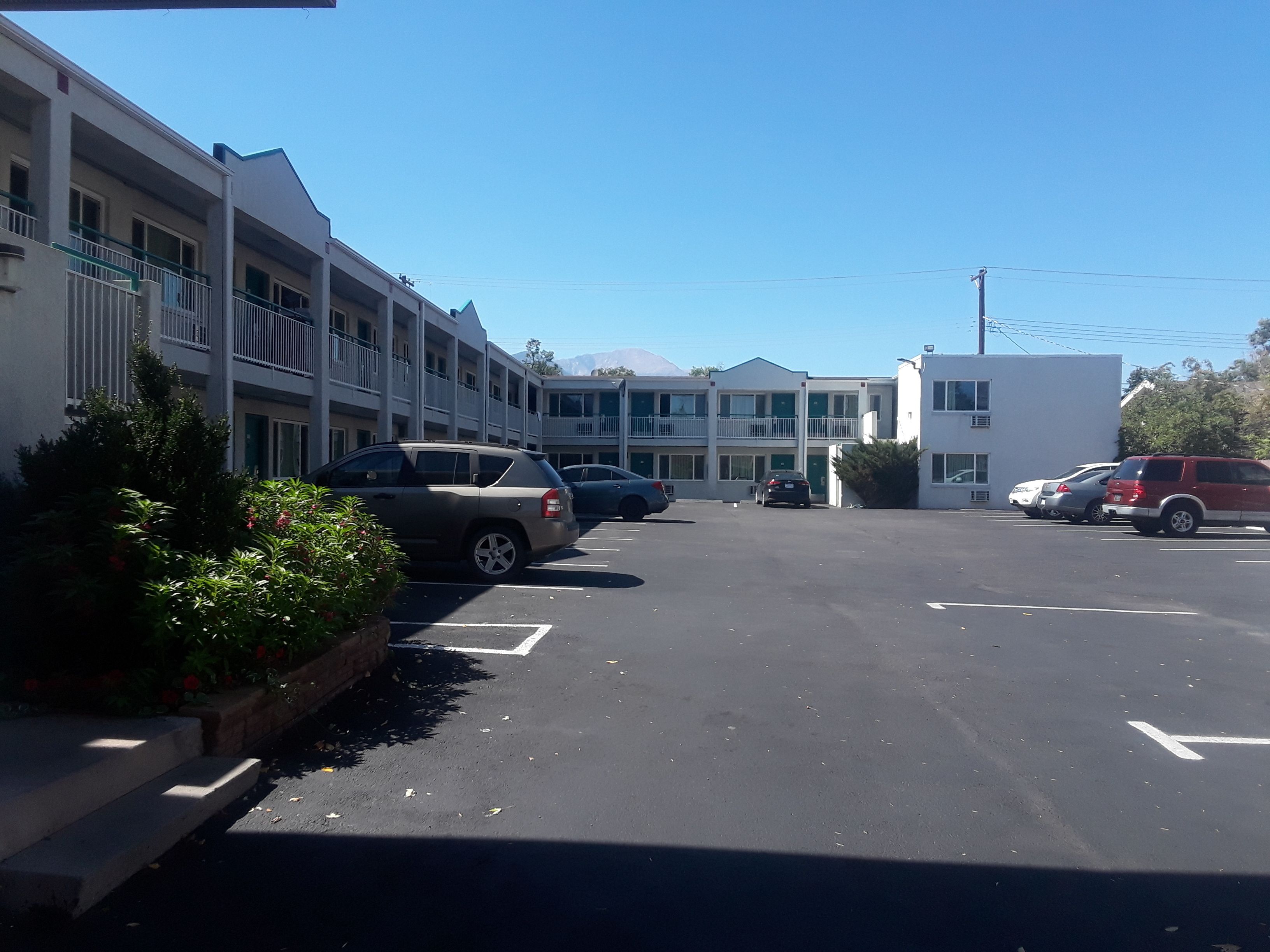 A parking lot with several cars, a building with balconies, and a clear blue sky.