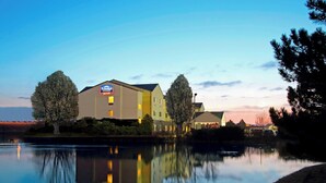 A hotel with a sign indicating it is a Fairfield Inn. It is situated beside a calm body of water with reflections of the building and trees. - Fairfield Inn & Suites by Marriott Colorado Springs South (Colorado Springs)