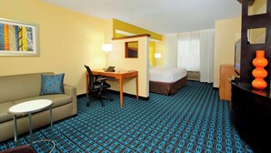 A hotel room with a sofa, a small table, a desk, a bed, and a television. - Fairfield Inn & Suites by Marriott Colorado Springs South (Colorado Springs)