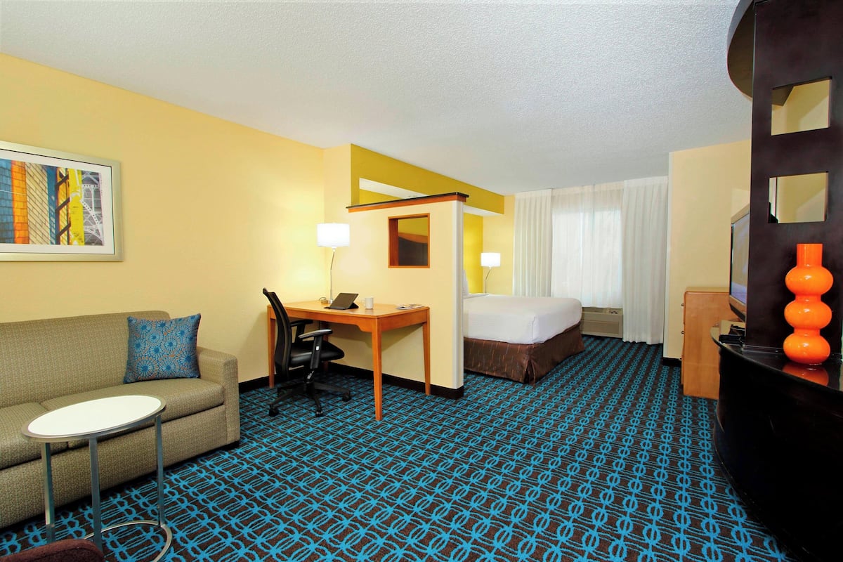 A hotel room with a sofa, a small table, a desk, a bed, and a television.