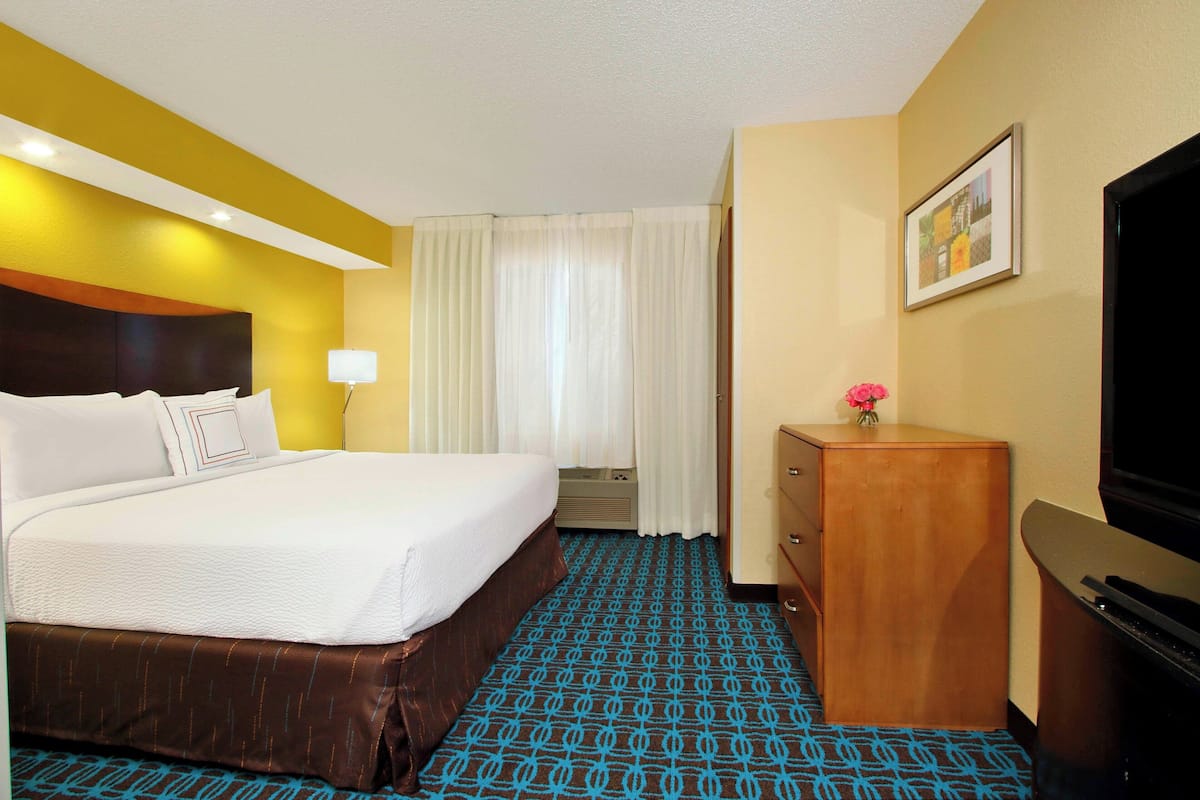 A hotel room with a large bed, a wooden dresser, a television, and a window with curtains.