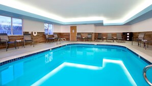 An indoor swimming pool with a tiled edge, surrounded by lounge chairs and a wooden accent wall. - Fairfield Inn & Suites by Marriott Colorado Springs South (Colorado Springs)