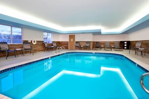 Una piscina interior con borde de azulejos, rodeada de sillas de descanso y una pared decorativa de madera.