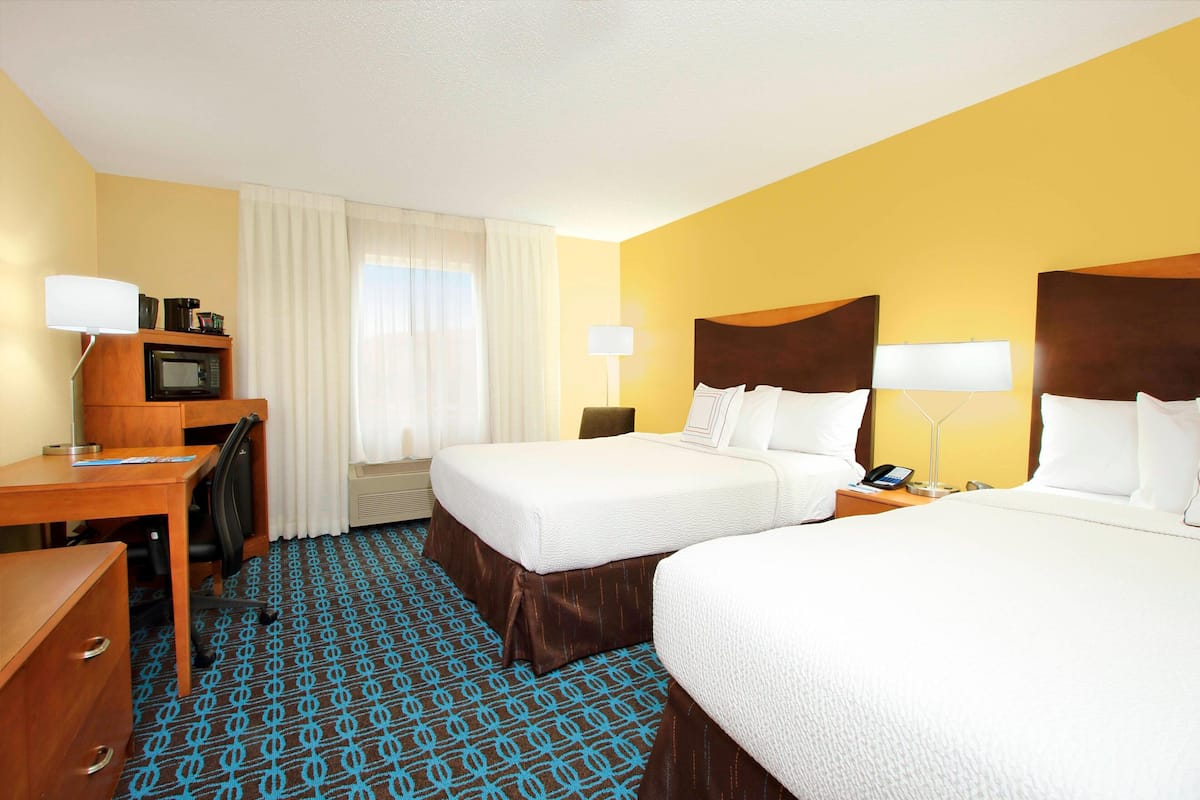 A hotel room with two beds, a desk, a chair, a microwave, and a telephone.
