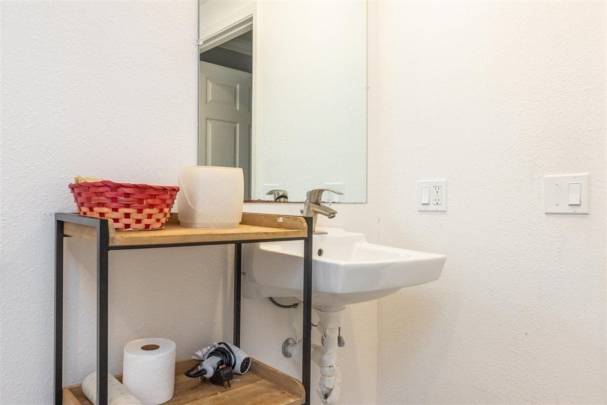 A bathroom with a white sink, a mirror, a wooden shelf with a basket, and a toilet paper roll.