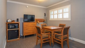 A compact kitchen with a microwave, coffee maker, and a TV on a wooden cabinet. There is a dining table with four chairs and a window with blinds. - SOMA Park Inn – Civic Center (San Francisco)