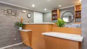 A reception area with a wooden counter, marble-topped sinks, a clock, and a mirror. - SOMA Park Inn – Civic Center (San Francisco)