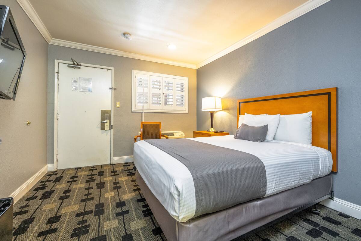 Una camera d'albergo con un letto, una scrivania, una sedia, una lampada e una porta.