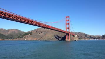 A red suspension bridge over a body of water with hills in the background.
