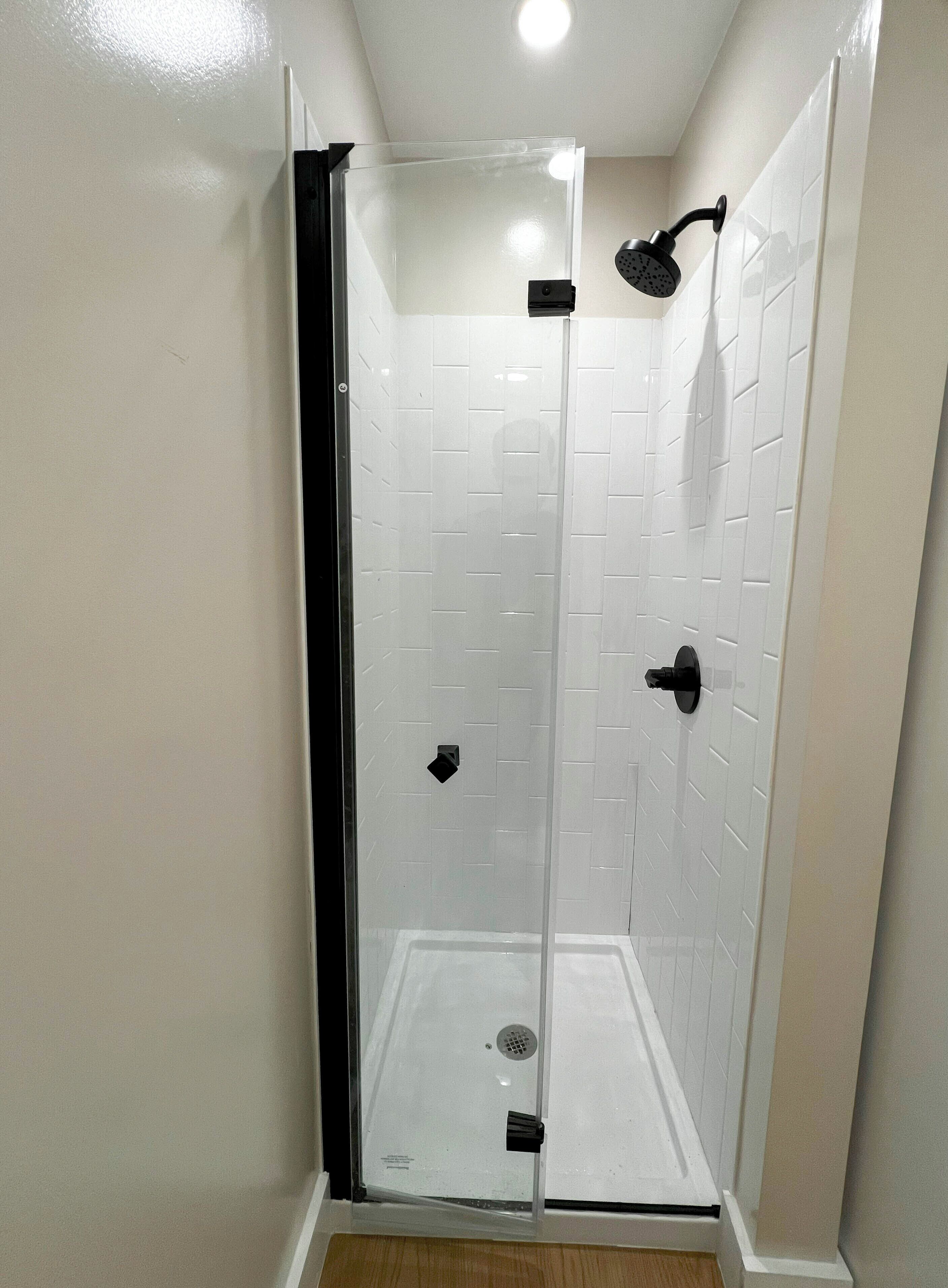 Un box de ducha con paredes de azulejos blancos y un cabezal de ducha negro.