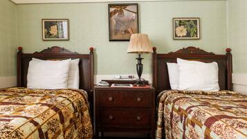 A room with two beds, each with a patterned bedspread, a nightstand with a lamp, and framed botanical prints on the wall.