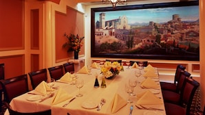 A dining room with a large table set for a meal, a ceiling fan, and a painting of a cityscape on the wall. - San Remo Hotel (San Francisco)