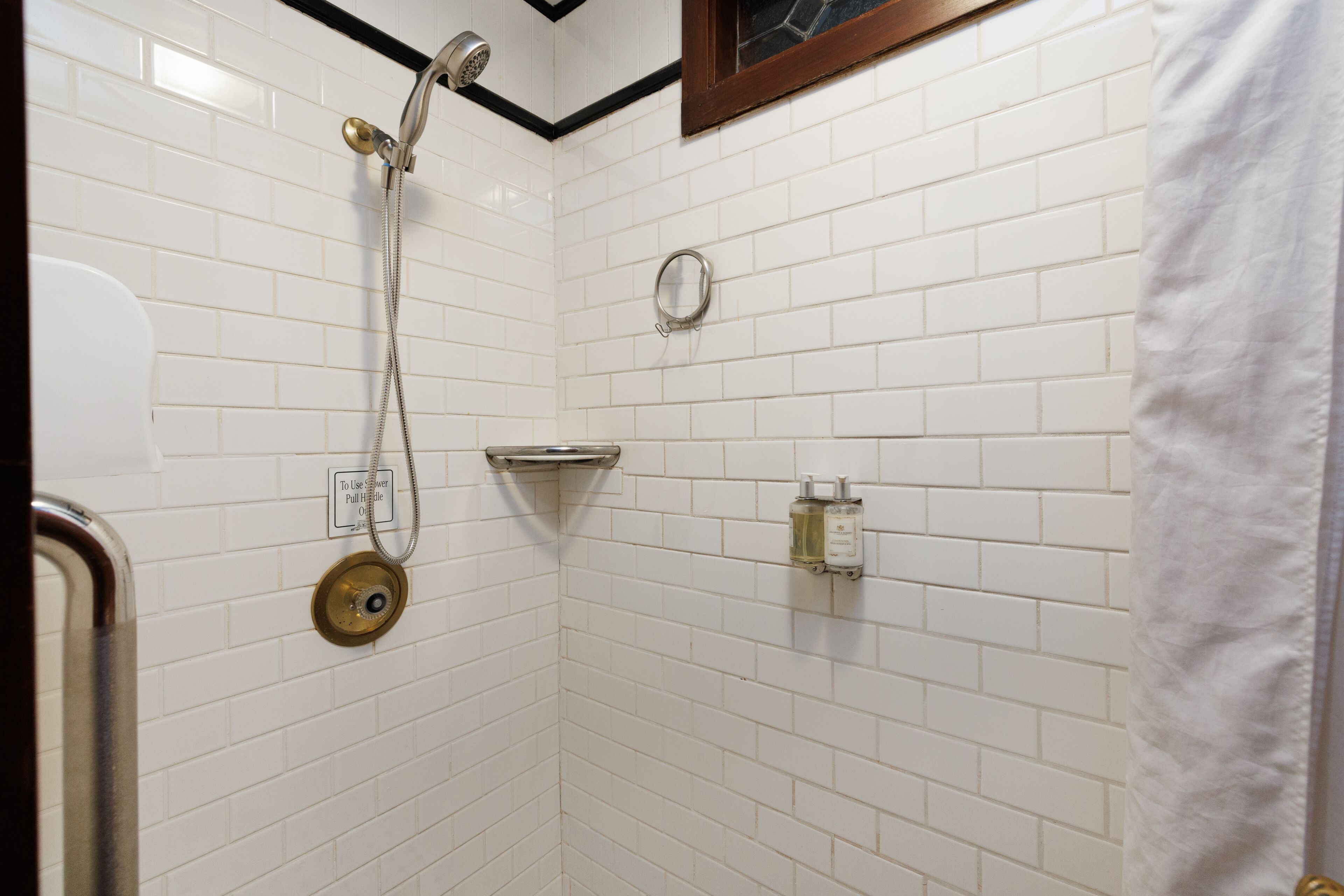 A bathroom with white subway tiles, a shower with a handheld showerhead, a towel rack, and a soap dispenser.