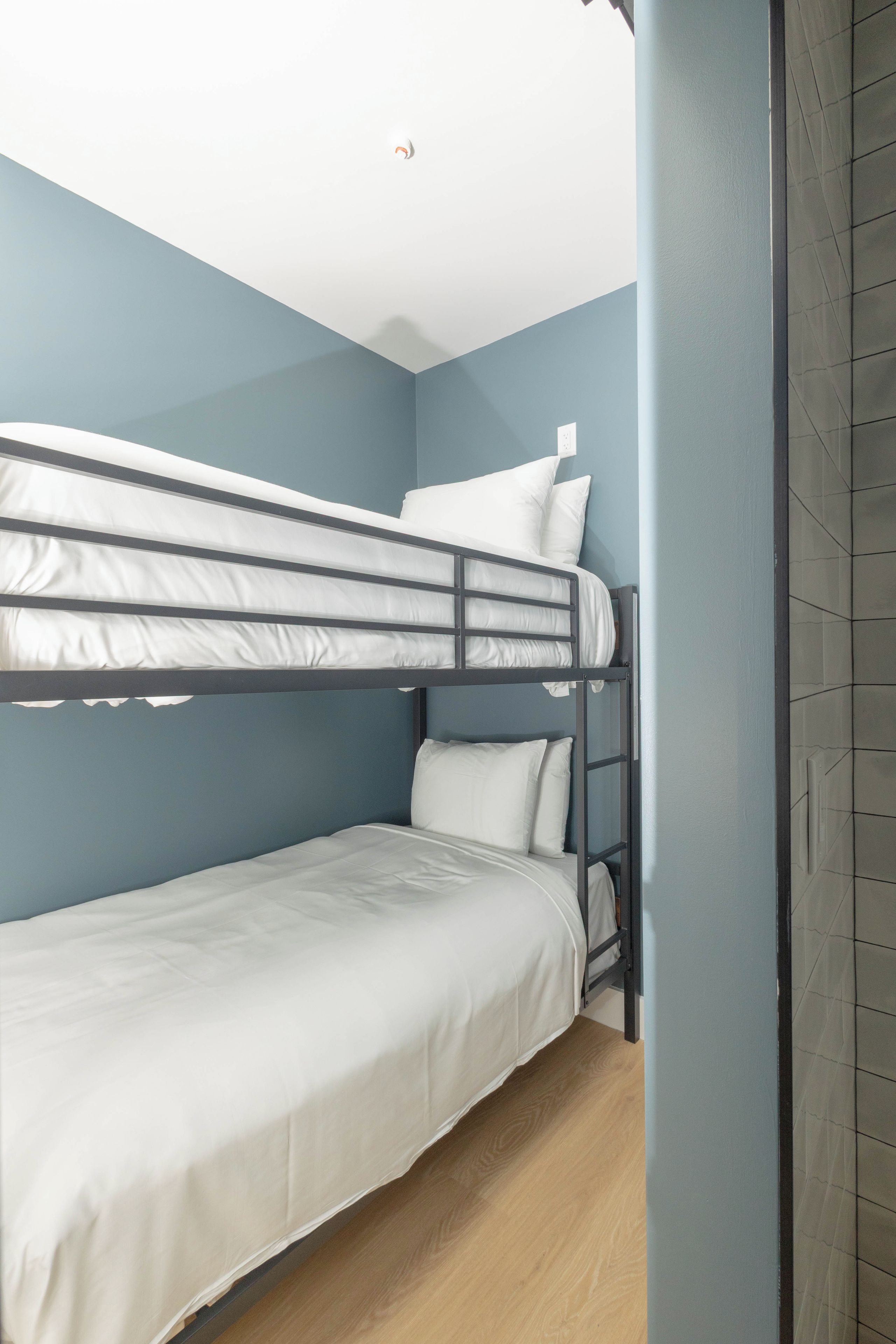 Een slaapkamer met stapelbedden, een houten vloer, een lichtblauwe muur en een wit plafond.
