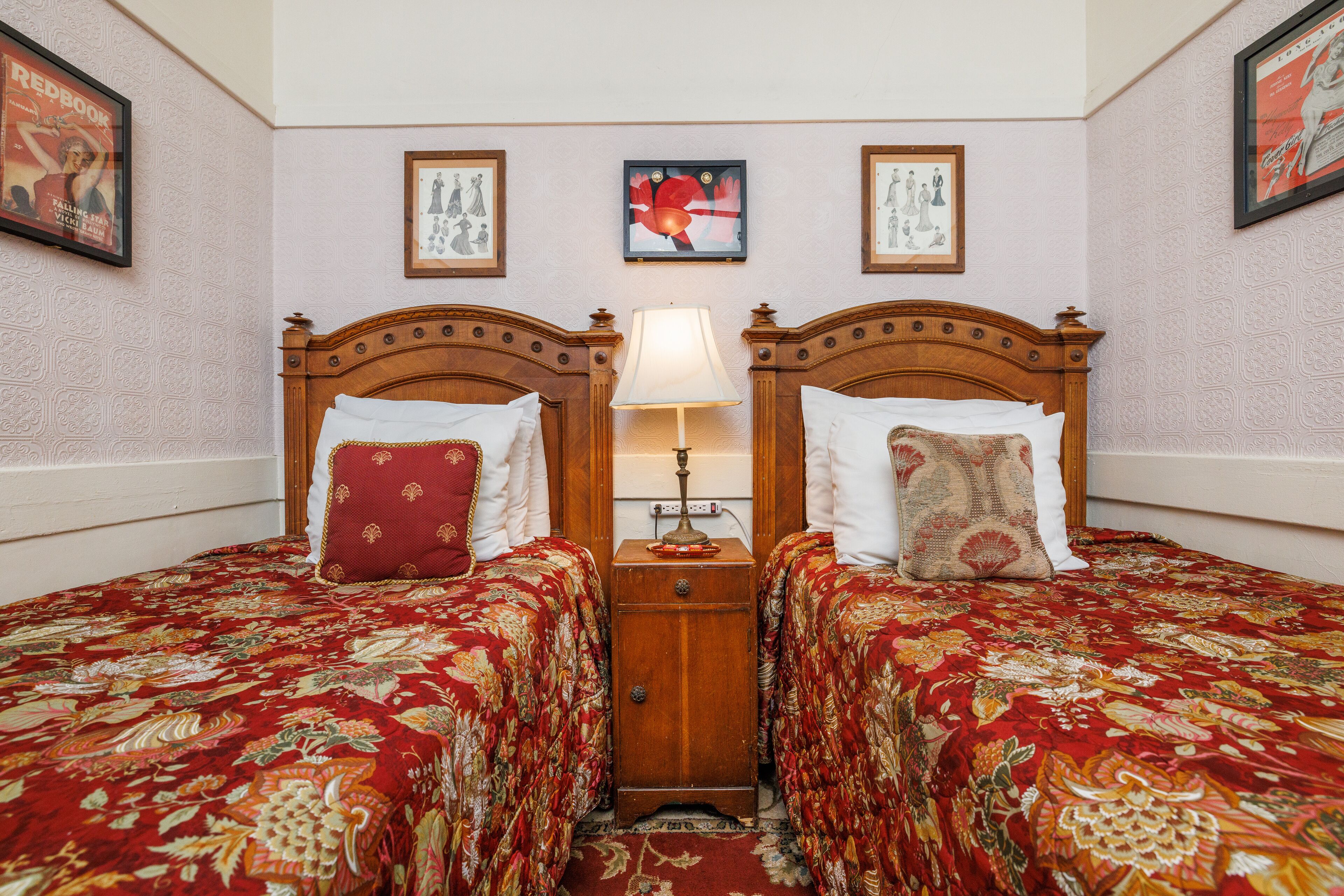 A hotel room with two beds, each with a floral bedspread, a nightstand with a lamp, and framed artwork on the walls.