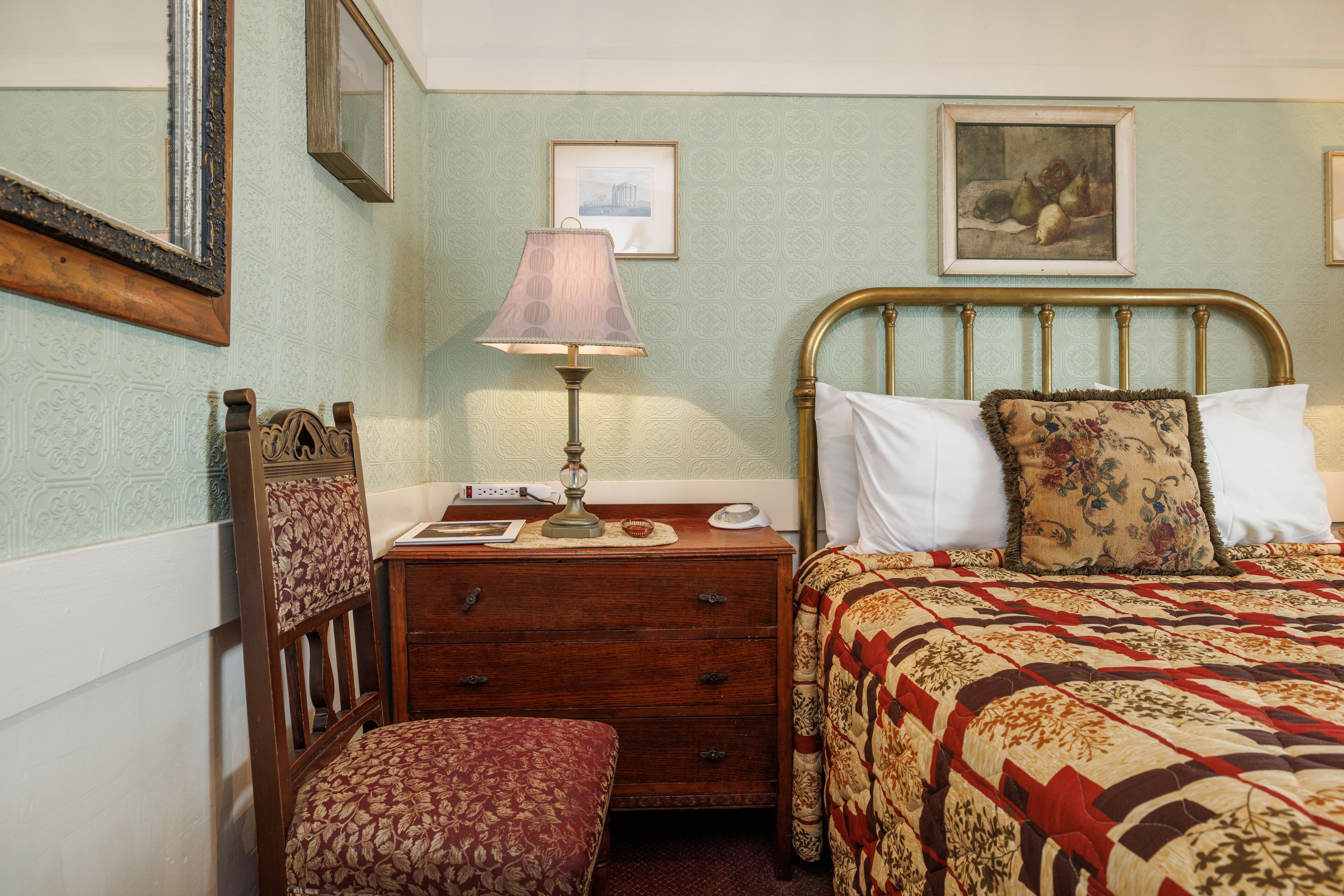 Un dormitorio ordenado con una mesita de noche de madera, una lámpara, una cama con edredón estampado y dos cuadros en la pared.