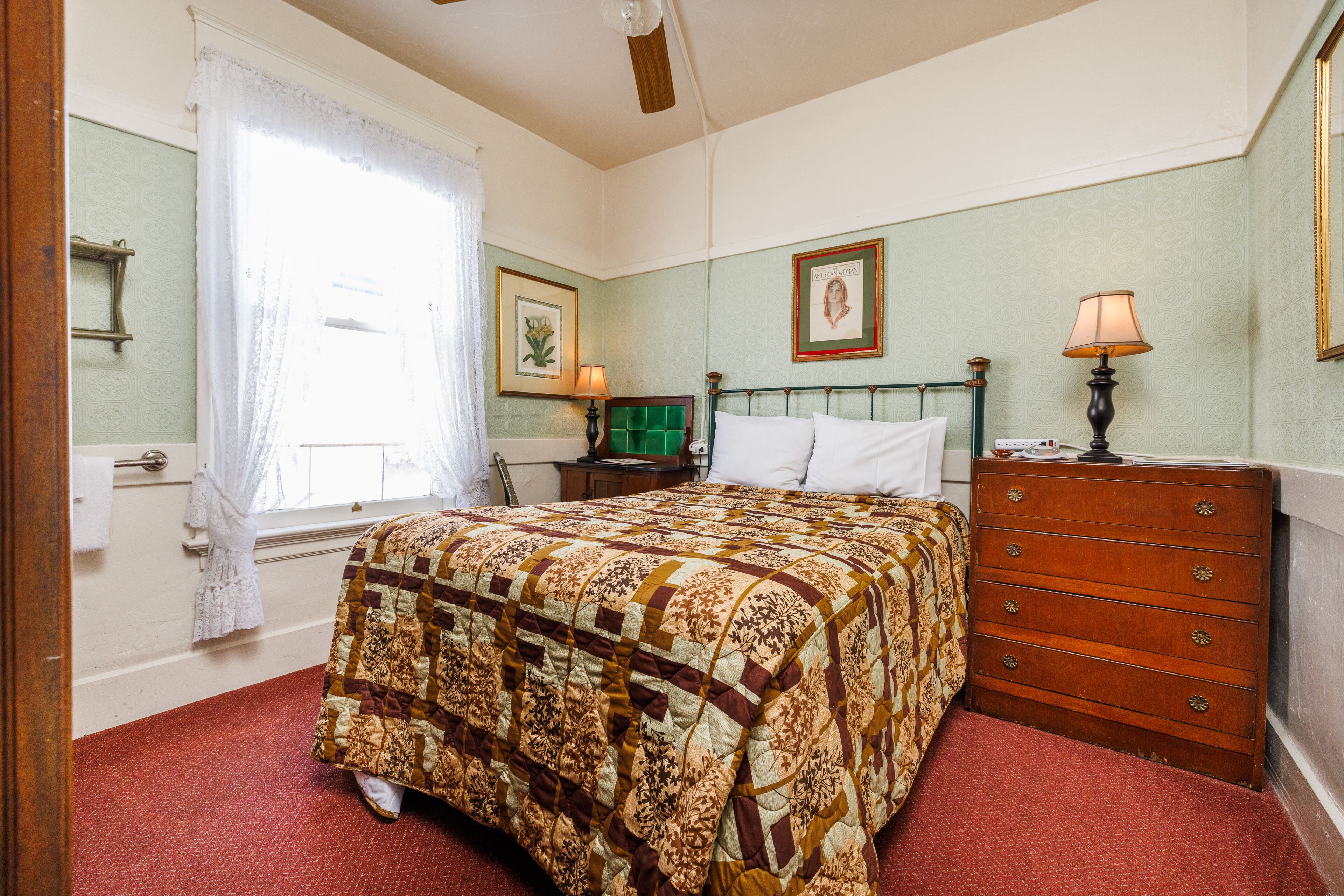 A bedroom with a bed, dresser, nightstand, and a window with curtains.
