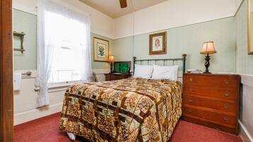 A bedroom with a bed, dresser, nightstand, and a window with curtains.